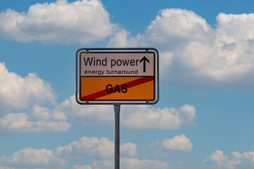 A sign with the text wind power and an arrow pointing up over the crossed-out word gas against a cloudy sky