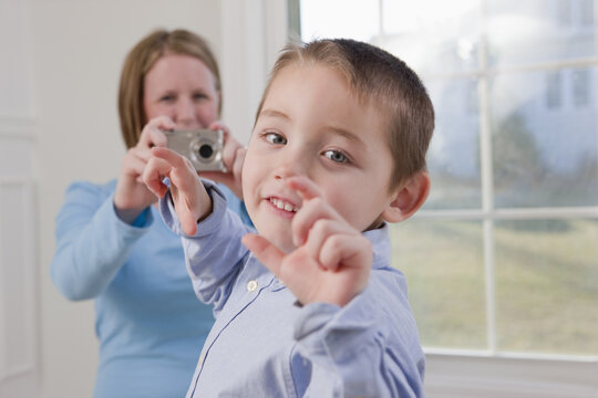 Boy signing the word 'Picture' in American Sign Language while his mother taking a picture of him with a digital camera