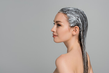 side view of cheerful young woman with bare shoulders and hair mask isolated on grey