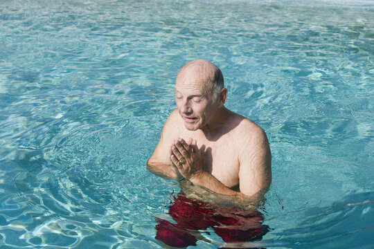 Senior man praying in a swimming pool, Florida, USA