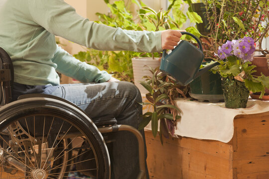 Woman with multiple sclerosis in a wheelchair watering houseplants