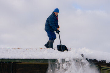 Man in action on the private house roof with shovel cleaning snow. Danger job.