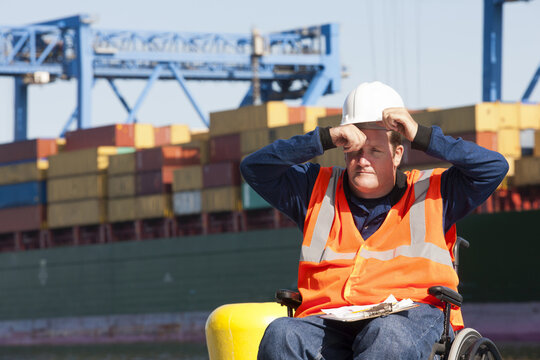 Transportation engineer in a wheelchair recording data for shipping containers and experiencing hot sun