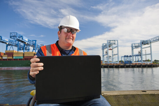 Transportation engineer in wheelchair recording data on laptop at shipping port