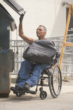 Loading dock worker with spinal cord injury in a wheelchair putting a bag in the dumpster