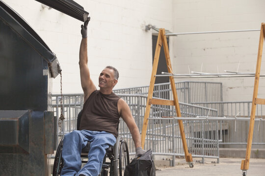 Loading dock worker with spinal cord injury in a wheelchair putting a bag in the dumpster