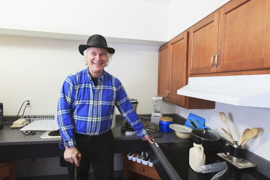 Man With Multiple Sclerosis Standing In His Accessible Kitchen With A Cane