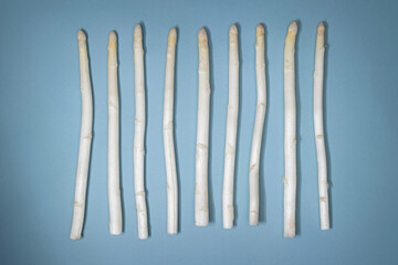 White asparagus in a line on blue- gray background with shadow