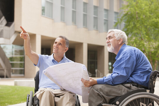 Design engineers reading Plans, one with muscular dystrophy and one with a spinal cord injury