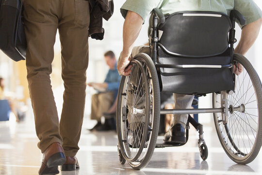Man with Muscular Dystrophy in a wheelchair walking with another passenger in a corridor of an airport