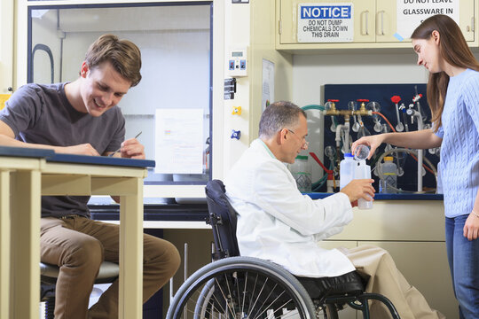 Professor with a spinal cord injury in a wheelchair working with students in an engineering lab filling container with distilled water