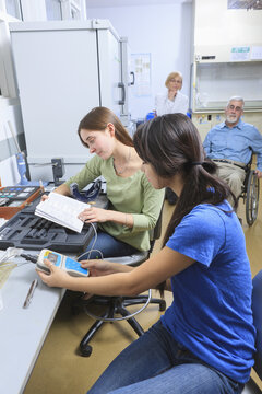 Engineering students working on a chemical analysis kit with professors in background, one with Muscular Dystrophy