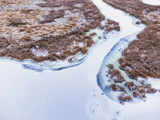Aerial view of a frozen riverbed with dry reeds on the bank.