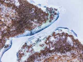Aerial top down view of frozen river channel with dry swamp grass.