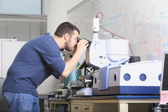 Engineering student looking through optical microscope on chemical analysis equipment in a laboratory