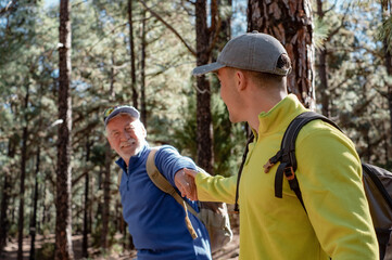 Fototapeta premium Happy and carefree couple of grandfather and teenager grandson hiking in the mountains sharing same passion for nature and healthy lifestyle together in the woods. Adventureisageless