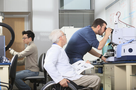 Professor with muscular dystrophy working with engineering student looking into x-ray fluorescence analyzer in a laboratory