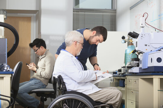 Professor with muscular dystrophy working with engineering student studying book for the x-ray fluorescence analyzer in a laboratory
