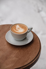 A cup of cappuccino with rose on top on wooden table. Table on the snow.