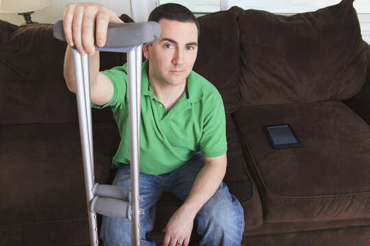 Man after anterior cruciate ligament (ACL) surgery with crutches and an digital tablet at home