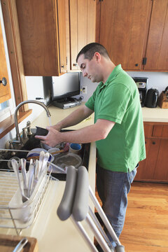 Man after anterior cruciate ligament (ACL) surgery with crutches washing dishes in the kitchen
