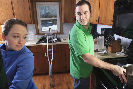 Man after anterior cruciate ligament (ACL) surgery with crutches cooking in the kitchen with wife