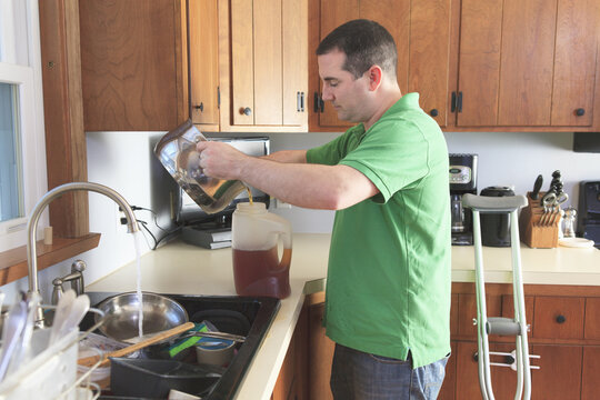 Man after anterior cruciate ligament (ACL) surgery with crutches making tea and doing dishes in the kitchen