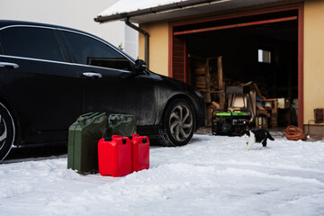 Four canisters with gasoline stand in snow against car.