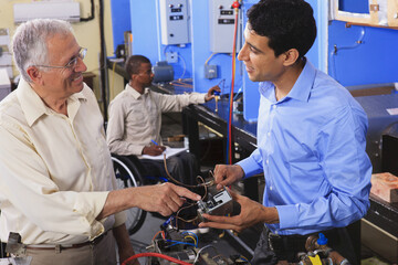 Student examining electrical control system on furnace with professor in HVAC classroom one student in wheelchair