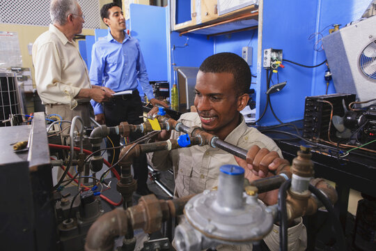 Student in wheelchair examining fuel control valves on furnace in HVAC classroom
