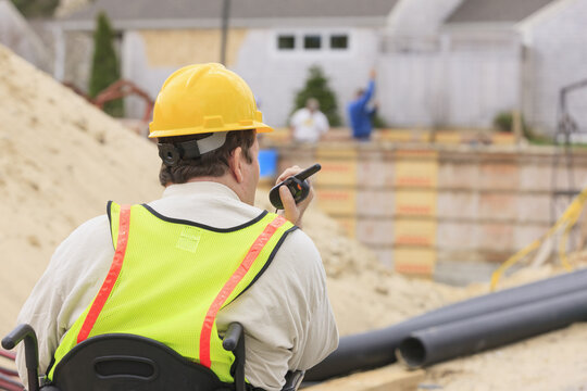 Construction supervisor with Spinal Cord Injury on walkie talkie with foundation and pipes in background