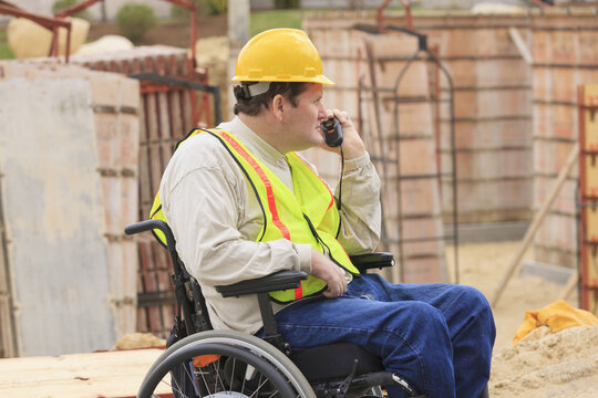 Construction supervisor with Spinal Cord Injury on walkie talkie inspecting concrete foundation forms
