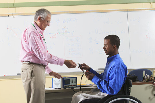 Electronics Professor demonstrating LCR impedance meter to student in wheelchair from Spinal Meningitis