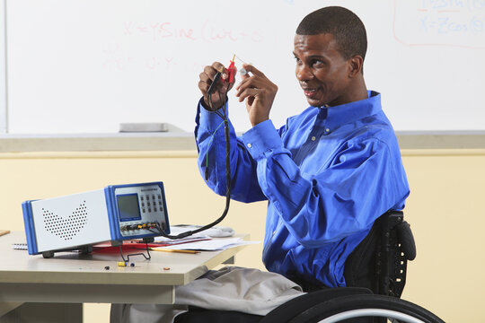 Engineering student in wheelchair from Spinal Meningitis connecting capacitor to LCR impedance meter