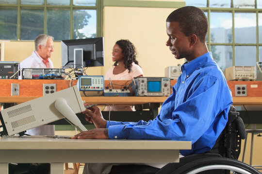 Engineering students in an electronics classroom, one in a wheelchair adjusting an oscilloscope
