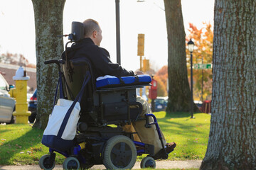 Man with spinal cord injury and arm with nerve damage in motorized wheelchair in a public park
