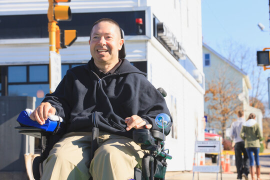Man with spinal cord injury and arm with nerve damage in motorized wheelchair crossing public street while shopping