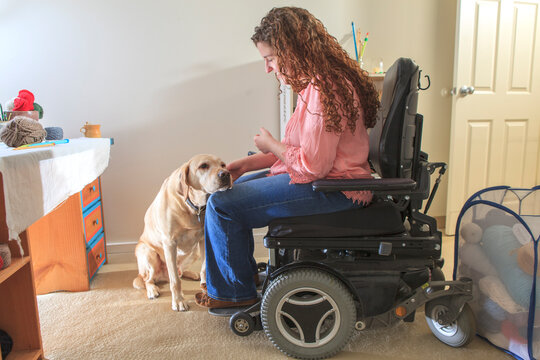 Woman with Muscular Dystrophy patting her service dog in her office