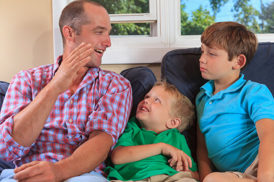 Father and sons with hearing impairments signing 'B' in American sign language on their couch