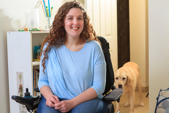 Woman with Muscular Dystrophy in her power chair with her service dog behind her
