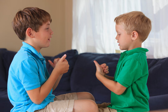 Boys with hearing impairments signing 'sports' in American sign language on their couch