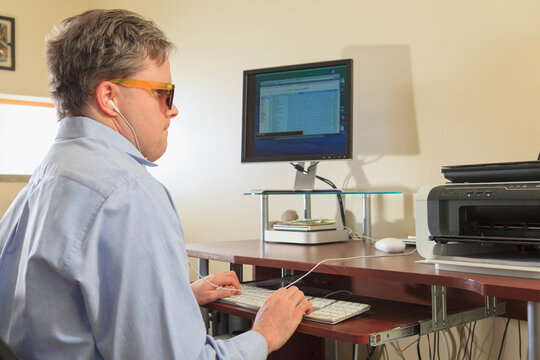 Man with congenital blindness using assistive technology at his computer to listen