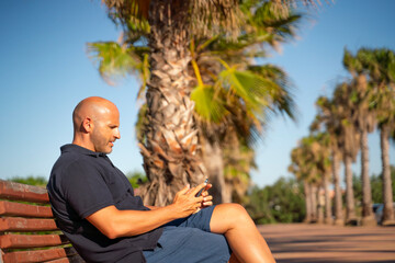 Bald man talking and using his smartphone in a tropical country