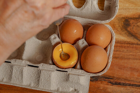 woman beating an egg in its own shell with a small mixer.
