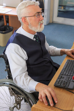 Man with Muscular Dystrophy in a wheelchair working at his computer in an office