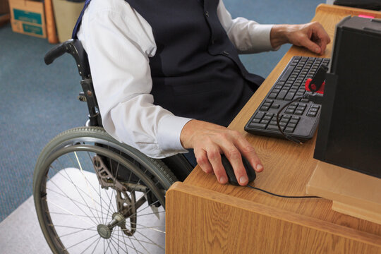 Man with Muscular Dystrophy in a wheelchair working at his computer in an office