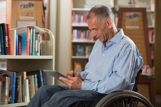 Man with a Spinal Cord Injury in a library reading a tablet