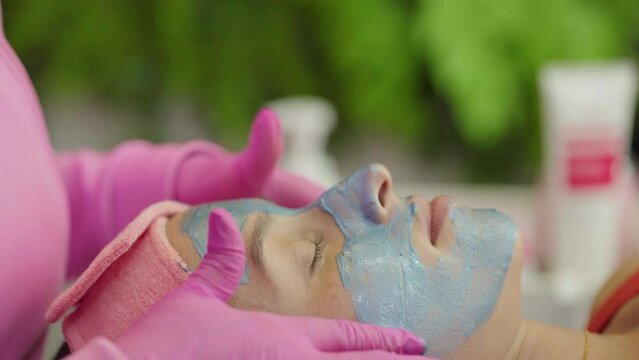 Close-up shot of a woman enjoying facial treatment with clay mask at beauty shop. Cosmetology and spa
