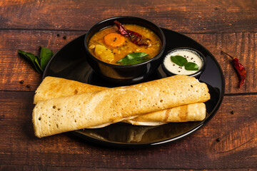 Crispy Dosa or Little Millet Dosa on a black plate. Served with sambar and chutney. Dosa is a popular South India and Sri Lanka cuisine. Shot on wooden background.