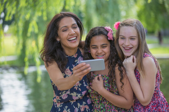 Happy Hispanic mother with two teen daughters with braces looking at text messages on mobile phone in park